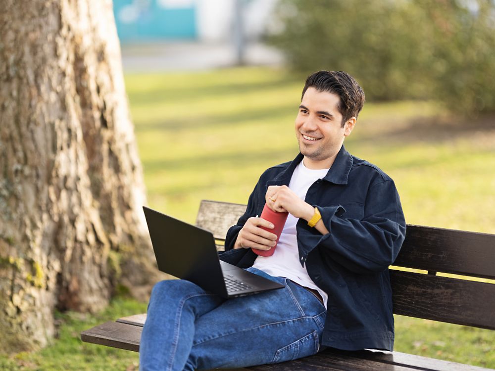 Henkelin työntekijä istuu penkillä puistossa ja työskentelee kannettavalla tietokoneella. 