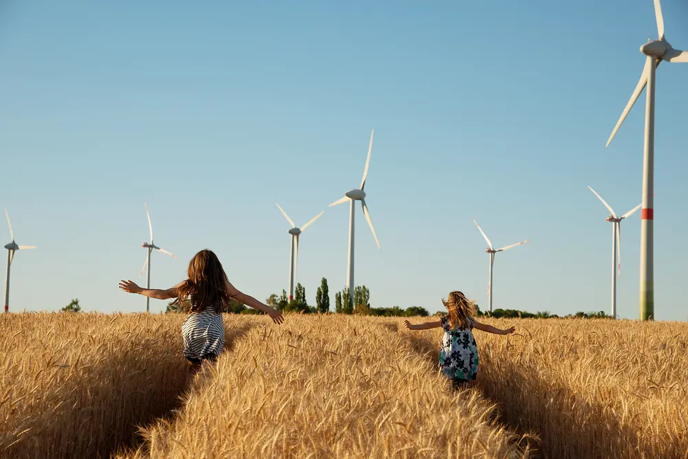 Tytöt juoksevat pellolla kohti tuulivoimaloita.