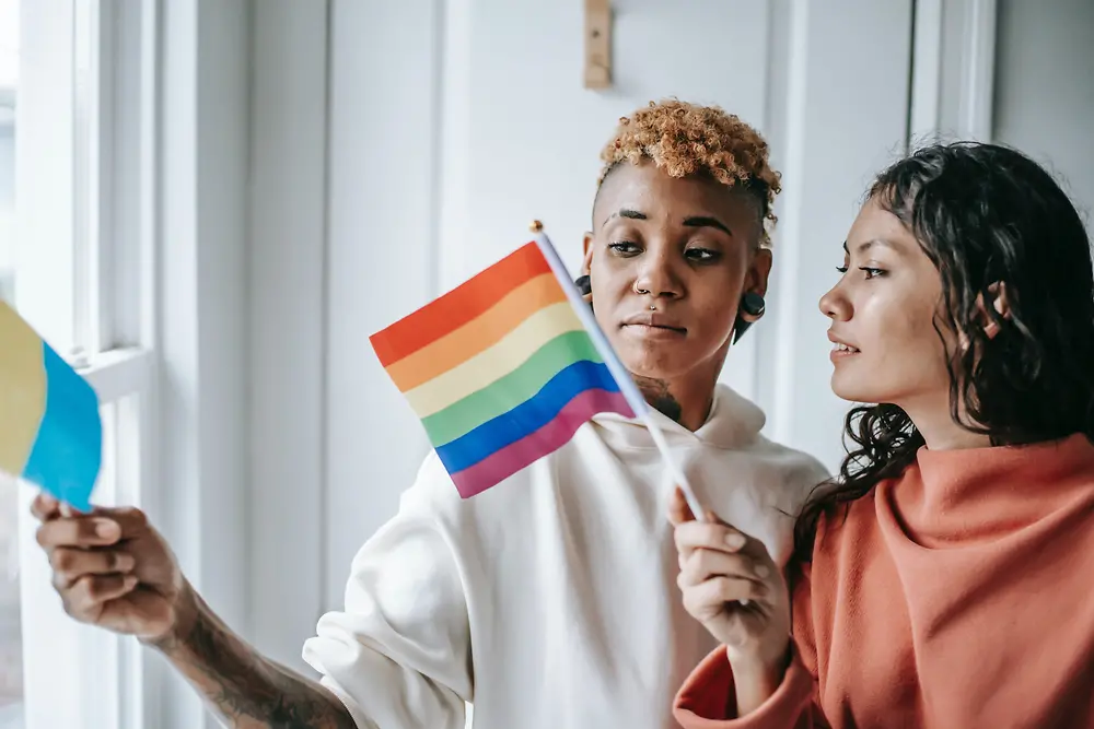 Kaksi naista keskustelee pitäen LGBTQ+ lippua.